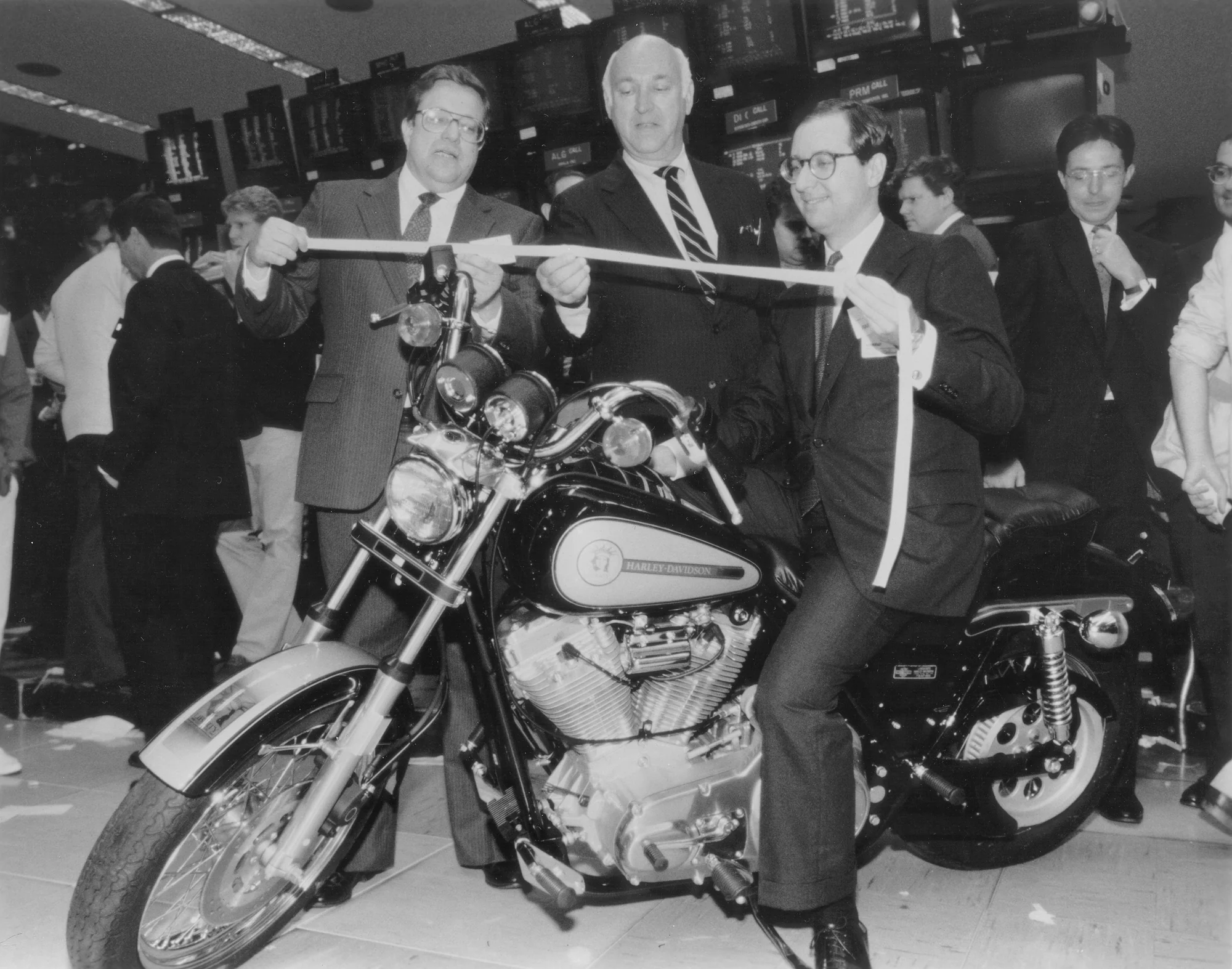 Vaughn Beals and Rich Teerlink at New York Stock Exchange holding ticker tape. Steve Delhi of Eaglemark is sitting on a Liberty Edition motorcycle.